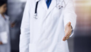 Bilinmeyen bir adam-doktor ayakta duruyor ve modern klinikte yardım eli uzatıyor. Kadın meslektaşının doktor geçmişinde acelesi var. Tıp konsepti