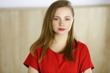 Zeki, kendinden emin, gülümseyen, Avrupalı bir kadının kollarını kavuşturup evinde dikilirken çekilmiş bir fotoğrafı. Çekici genç kız öğrenci serbest çalışan, kırmızı giyinmiş, kameraya bakıyor.