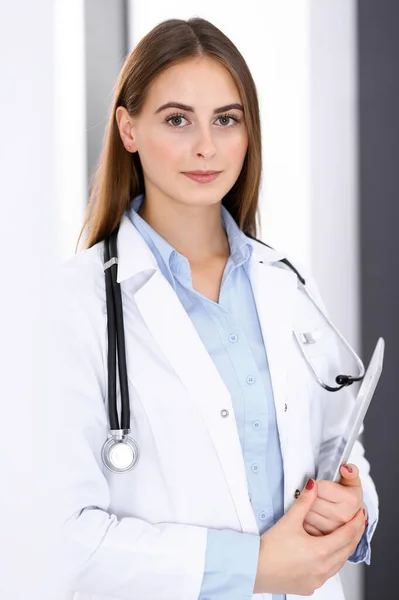 Mujer doctora usando tableta mientras está de pie cerca de la ventana en el hospital. Feliz médico en el trabajo. Concepto de medicina y salud — Foto de Stock