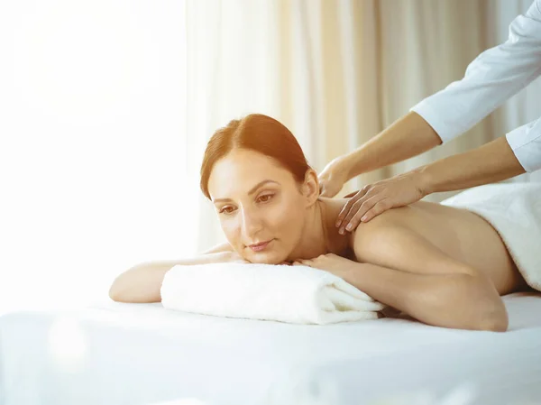 Ganska brunett kvinna njuter av proceduren med ryggmassage i solig spa salong. Skönhetskoncept. Kalltonad bild — Stockfoto