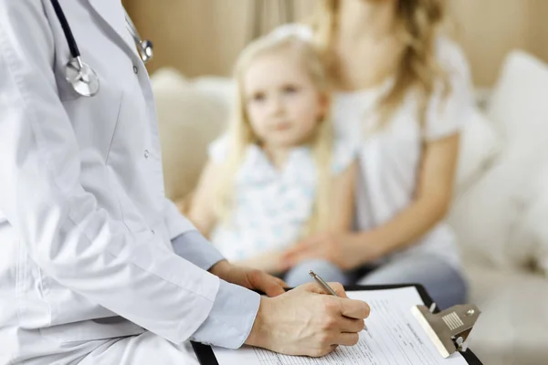 Doctor and patient. Pediatrician using clipboard while examining little girl with her mother at home. Happy cute caucasian child at medical exam. Medicine concept — Stock Photo, Image