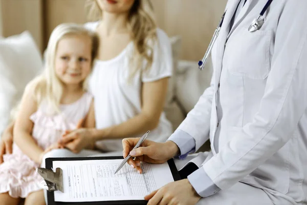 Doctor and patient. Pediatrician using clipboard while examining little girl with her mother at home. Happy cute caucasian child at medical exam. Medicine concept — Stock Photo, Image