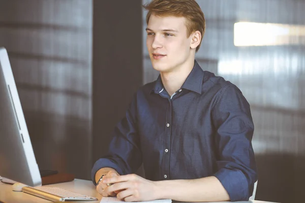 Jeune homme d'affaires blond réfléchissant à la stratégie à son lieu de travail avec ordinateur. Démarrage d'entreprise signifie travailler dur et hors du temps pour la réussite — Photo