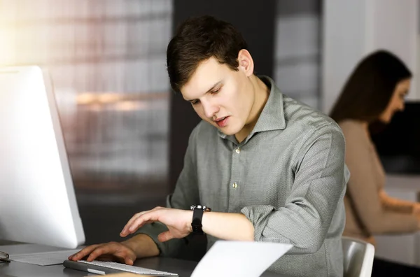 Der junge Geschäftsmann sitzt am Schreibtisch im Büro und arbeitet an seinem Computer. Kopfschuss-Porträt eines Mannes — Stockfoto