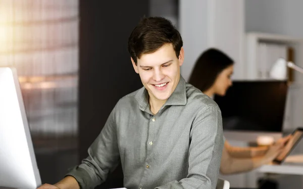 Молодой бизнесмен, работающий за компьютером, сидит за столом в офисе. Хедшот портрет человека — стоковое фото