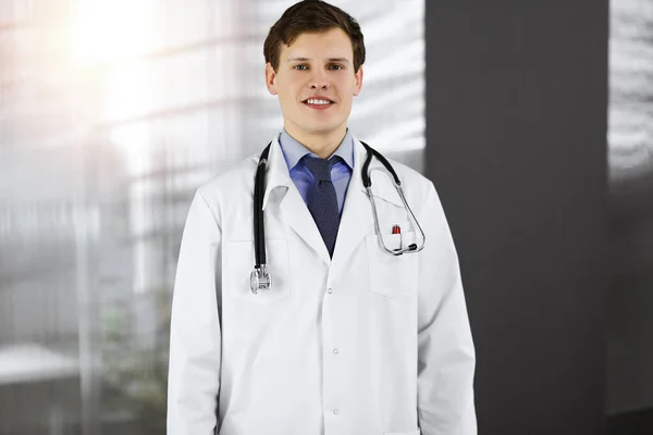 Un jeune médecin positif sourit à la caméra. Portrait de médecin professionnel en clinique ensoleillée — Photo