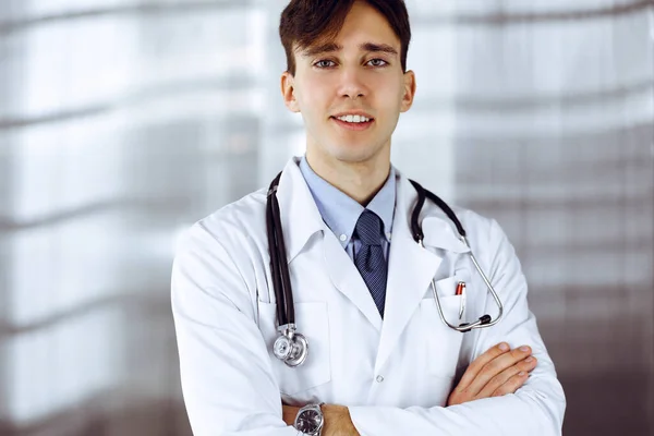 病院で腕を組んで立っている陽気な笑顔の医者。病院で若いスマート医師との完璧な医療サービス。医学の概念 — ストック写真