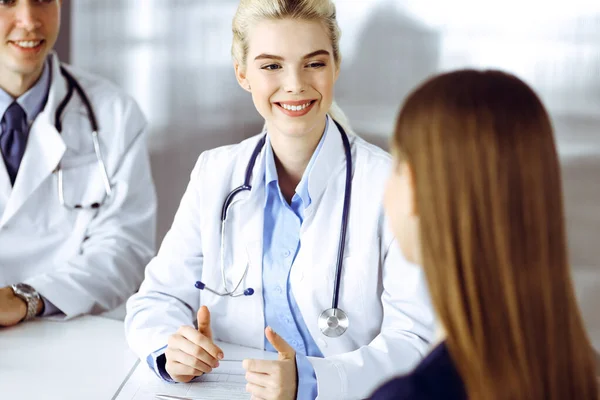 Ärztin und männlicher Kollege beraten die Patientin, während sie am Schreibtisch in der modernen Klinik sitzen. Perfekter medizinischer Service, medizinisches Konzept — Stockfoto