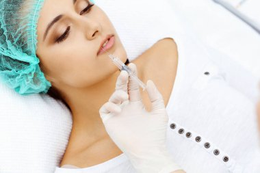 Profesyonel kozmetik uzmanı yüzüne ve dudaklarına iğne yapıyor. Genç bir kadın, yüz hatları ya da büyütme için doldurucu iğneyle doldurulur. Yaşlanma, gençleşme ve hidrasyon prosedürleriyle yüzleş