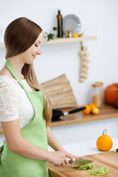 Mooie vrouw gekleed in een schort kookt eten in de keuken. Huisvrouw snijdt verse veganistische salade — Stockfoto