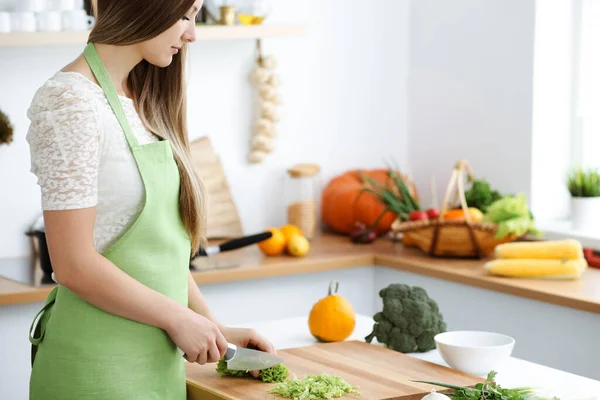 Mooie vrouw gekleed in een schort kookt eten in de keuken. Huisvrouw snijdt verse veganistische salade — Stockfoto