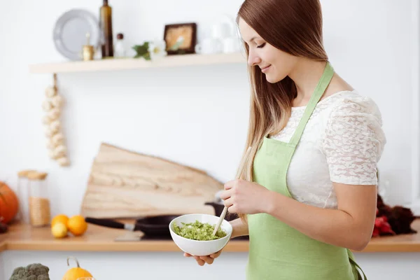 Mooie vrouw gekleed in een schort kookt eten in de keuken. Huisvrouw snijdt verse veganistische salade — Stockfoto