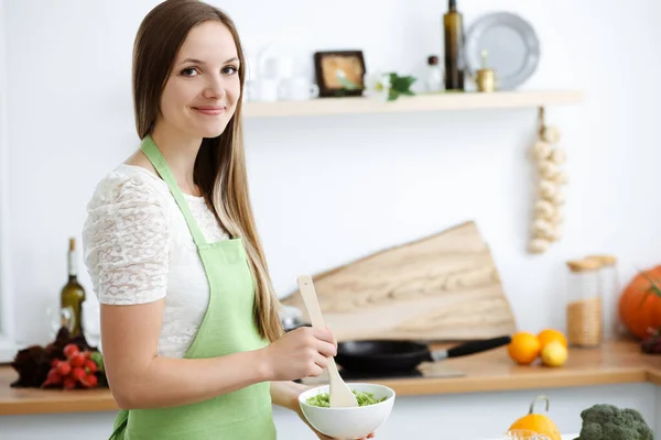 Όμορφη γυναίκα ντυμένη με ποδιά μαγειρεύει στην κουζίνα. Νοικοκυρά τεμαχίζει φρέσκια χορτοφαγική σαλάτα — Φωτογραφία Αρχείου