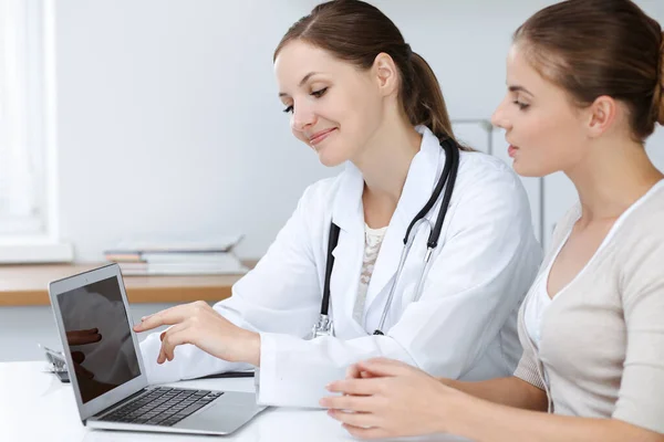 Médico e paciente estão sentados e discutindo os resultados do exame de saúde ao usar o computador portátil. Saúde, medicina e boas notícias conceitos — Fotografia de Stock