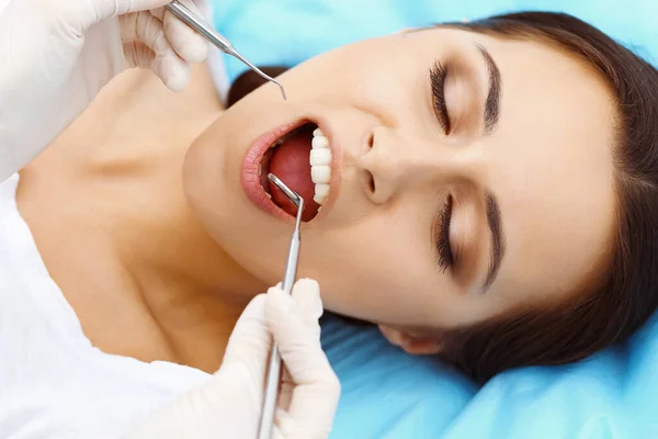Młoda pacjentka odwiedzająca gabinet stomatologiczny.Piękna kobieta ze zdrowymi, białymi zębami siedząca na krześle dentystycznym z otwartymi ustami podczas kontroli jamy ustnej, podczas gdy lekarz pracuje nad zębami — Zdjęcie stockowe