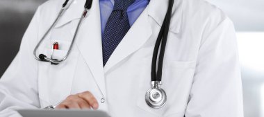 Klinikte dururken elinde tablet bilgisayar tutan kimliği belirsiz bir erkek doktor. Coronavirüs salgını sırasında ilaç kavramı