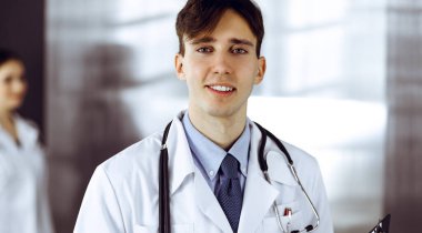 Modern klinikte dostane genç bir erkek doktor elinde bir panoyla dikiliyor. Bayan meslektaşım, doktorların arka planında ilaç kayıtları doldurmakla meşgul. Tıp konsepti