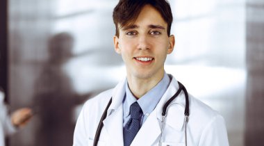 Modern klinikte dostane genç bir erkek doktor elinde bir panoyla dikiliyor. Bayan meslektaşım, doktorların arka planında ilaç kayıtları doldurmakla meşgul. Tıp konsepti