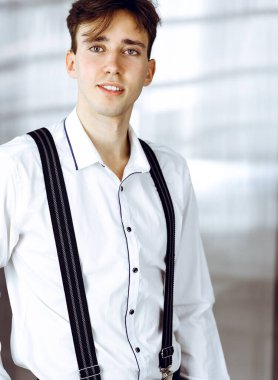 Modern ofiste beyaz gömlekli, dost canlısı genç bir işadamı duruyor.