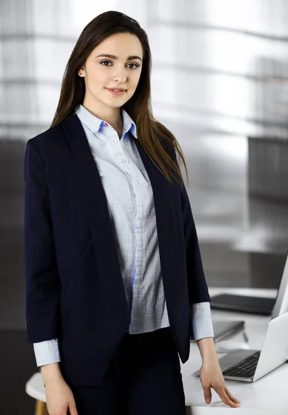 Una joven empresaria inteligente con una chaqueta azul está parada en su lugar de trabajo. Retrato de un especialista en una oficina moderna — Foto de Stock