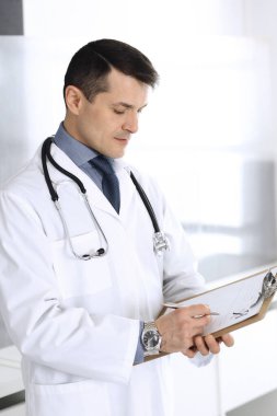 Doktor, ilaç kayıtlarını doldurmak için pano kullanıyor. Klinikte mükemmel bir tıbbi hizmet. Hastanede çalışan bir doktor. Tıp ve sağlık hizmetleri kavramları