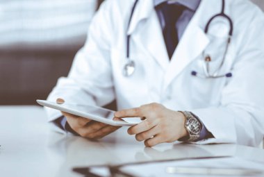 Bilinmeyen erkek doktor klinikteki tablet bilgisayarla yakın planda çalışıyor. İşteki genç doktor. Mükemmel sağlık hizmeti, tıp konsepti