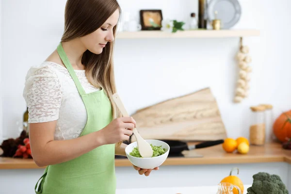 Mooie vrouw gekleed in een schort kookt eten in de keuken. Huisvrouw snijdt verse veganistische salade — Stockfoto
