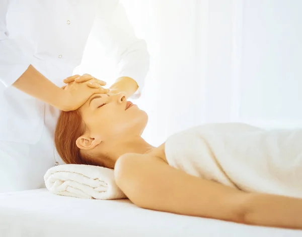 Piękna kobieta korzystająca z masażu twarzy z zamkniętymi oczami w słonecznym centrum spa. Relaksująca koncepcja leczenia w medycynie — Zdjęcie stockowe