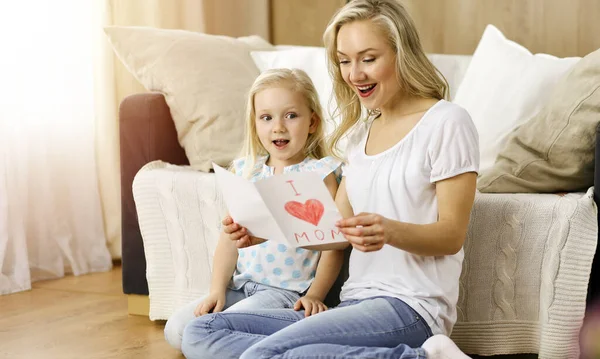 Happy mother day in sunny flat. Child daughter congratulates mom and gives her postcard with heart drawing. Family concept — Stock Photo, Image