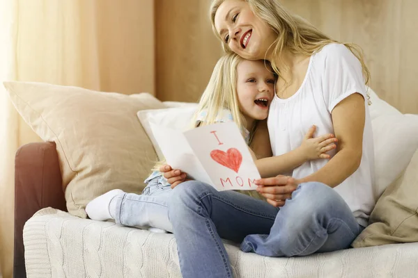 Happy mother day in sunny flat. Child daughter congratulates mom and gives her postcard with heart drawing. Family concept — Stock Photo, Image