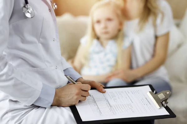 Doctor y paciente. Pediatra usando portapapeles mientras examina a la niña con su madre en casa. Niño enfermo e infeliz en el examen médico — Foto de Stock