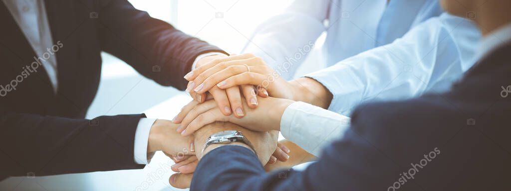 Business team showing unity with their hands together in sunny office. Group of people joining hands and representing concept of friendship, teamwork and partnership
