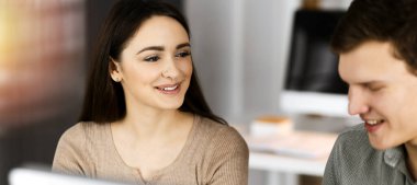 Dost canlısı genç iş kadını, modern bir ofiste erkek bir meslektaşıyla birlikte çalışıyor.