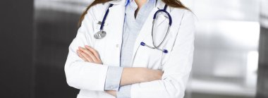 Kimliği belirsiz genç bir kadın doktor güneşli klinikte kollarını kavuşturmuş duruyor. Coronavirus salgını sırasında ilaç konsepti. Covid 2019