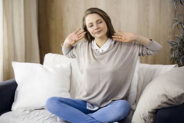 Mutlu esmer kadın ellerini başının arkasına koyuyor koltuğa yaslanıyor Avrupalı kadın tembel hafta sonunun keyfini çıkarıyor ya da sıcak oturma odasında tatilin tadını çıkarıyor, ev hanımı ev işi yaptıktan sonra rahatlıyor.