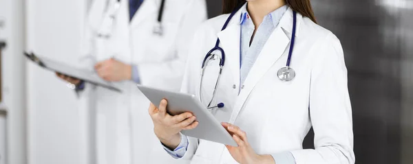 Okänd kvinnlig läkare använder tablettdator i händerna när hon står på kliniken. Medicinskt koncept under Coronavirus pandemi — Stockfoto