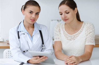 Doktor ve hasta tablet bilgisayar kullanırken oturup sağlık muayenesi sonuçlarını tartışıyorlar. Sağlık, ilaç ve iyi haber kavramları