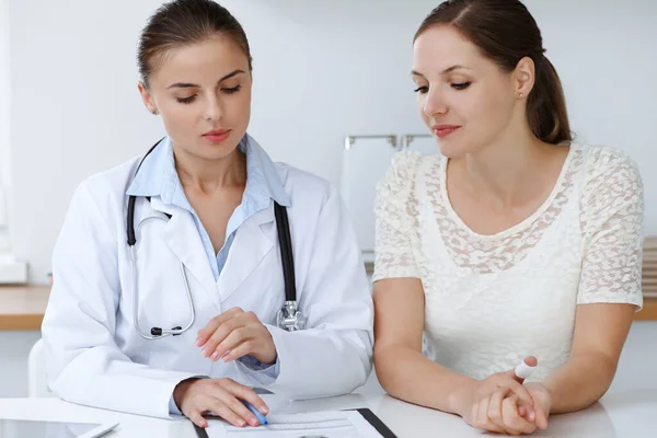 Doctor and patient sitting at the desk. The physician or therapist makes a diagnosis. Health care, medicine and patient service concept