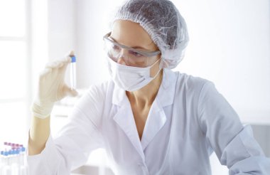 Koruyucu gözlüklü profesyonel kadın bilim adamı güneşli laboratuvarda reaktörlerle araştırma tüpü kullanıyor. Tıp ve bilim araştırmaları