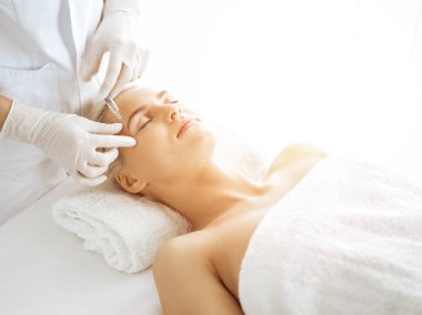 Güzellik uzmanı elleri güneşli klinikte kadın yüzüne şırınga ile güzellik prosedürü uyguluyor. Kozmetik tıp ve cerrahi, güzellik enjeksiyonları konsepti