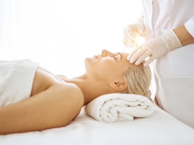 Güzellik uzmanı elleri güneşli klinikte kadın yüzüne şırınga ile güzellik prosedürü uyguluyor. Kozmetik tıp ve cerrahi, güzellik enjeksiyonları konsepti