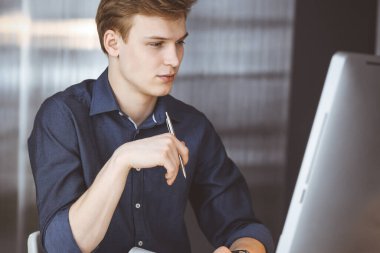 Genç sarışın işadamı iş yerinde bilgisayarla strateji düşünüyor. Girişim işi, başarı için çok çalışmak ve zamanın dışında çalışmak demektir.