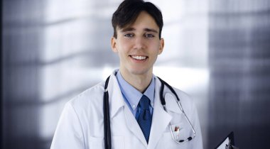 Modern klinikte dostane genç bir erkek doktor elinde bir panoyla dikiliyor. Bayan meslektaşım, doktorların arka planında ilaç kayıtları doldurmakla meşgul. Tıp konsepti