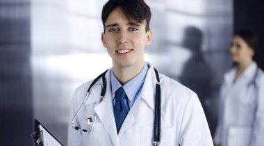 Modern klinikte dostane genç bir erkek doktor elinde bir panoyla dikiliyor. Bayan meslektaşım, doktorların arka planında ilaç kayıtları doldurmakla meşgul. Tıp konsepti