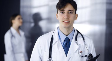 Modern klinikte dostane genç bir erkek doktor elinde bir panoyla dikiliyor. Bayan meslektaşım, doktorların arka planında ilaç kayıtları doldurmakla meşgul. Tıp konsepti