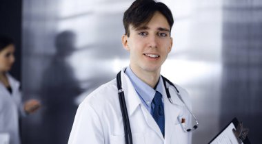 Modern klinikte dostane genç bir erkek doktor elinde bir panoyla dikiliyor. Bayan meslektaşım, doktorların arka planında ilaç kayıtları doldurmakla meşgul. Tıp konsepti