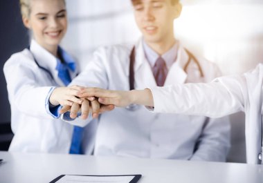 Çember olarak el ele tutuşan ve modern hastane ofisindeki masada otururken hastalara yardım etmeye hazır bir grup doktor. Tıpta başarılı takım çalışması, Coronavirus karşı koyma konsepti