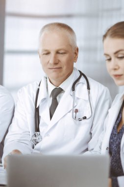 Doktorlar meslektaşları ve yaşlı terapist güneşli klinikte çalışırken güncel hastalık terapisini tartışıyorlar. Tıpta takım çalışması