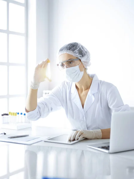 Científica profesional en gafas protectoras investigando tubo con reactivos en laboratorio soleado. Investigación en medicina y ciencia — Foto de Stock