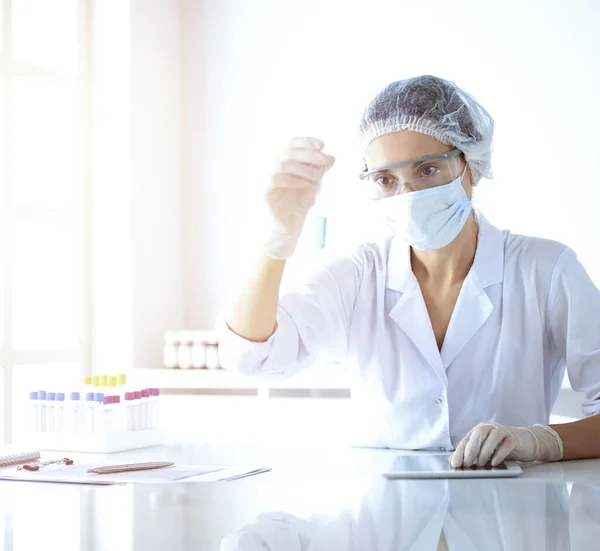 Científica profesional en gafas protectoras investigando tubo con reactivos en laboratorio soleado. Investigación en medicina y ciencia — Foto de Stock